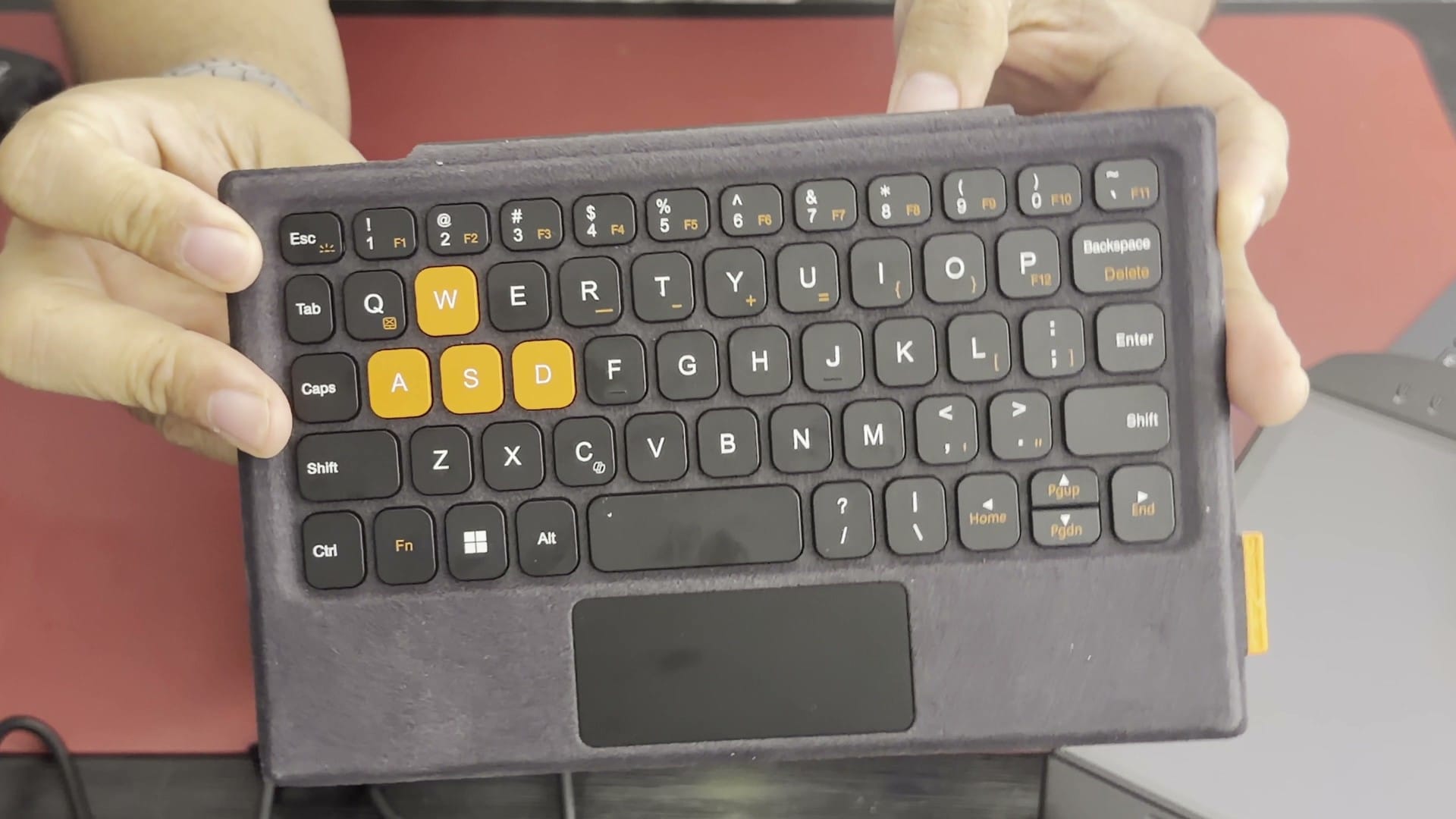 The OneXPlayer X2 Mini Pro keyboard held up, with orange WASD keys and a small trackpad