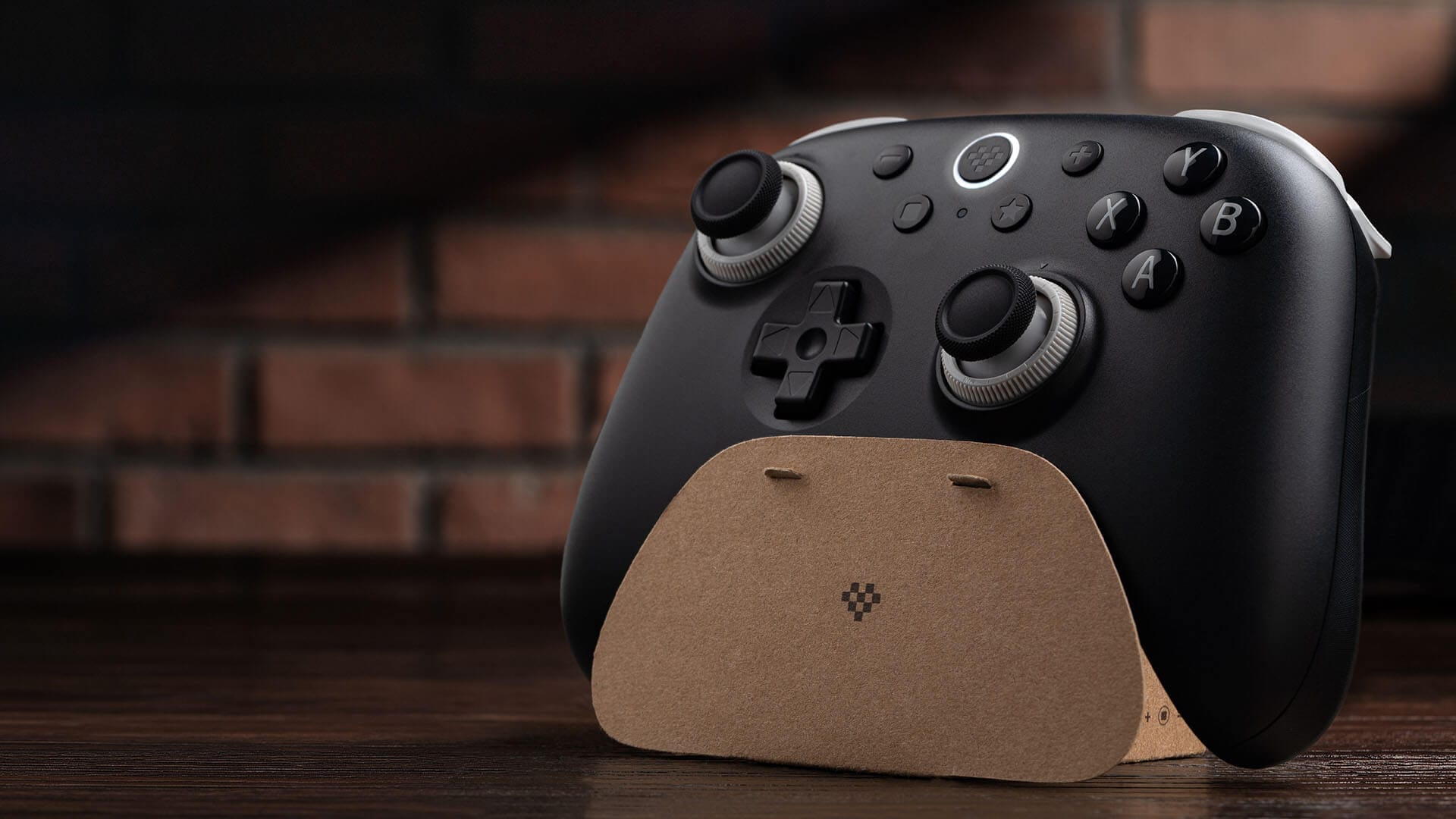 The black 8BitDo Ultimate 3C+ resting on its cardboard stand on a wooden desk