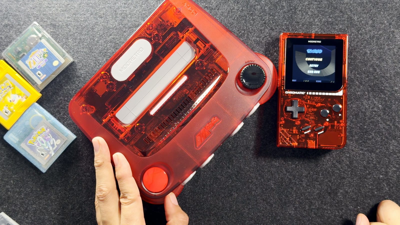 The transparent red Chromatic lying next to a transparent red ModRetro M64 console