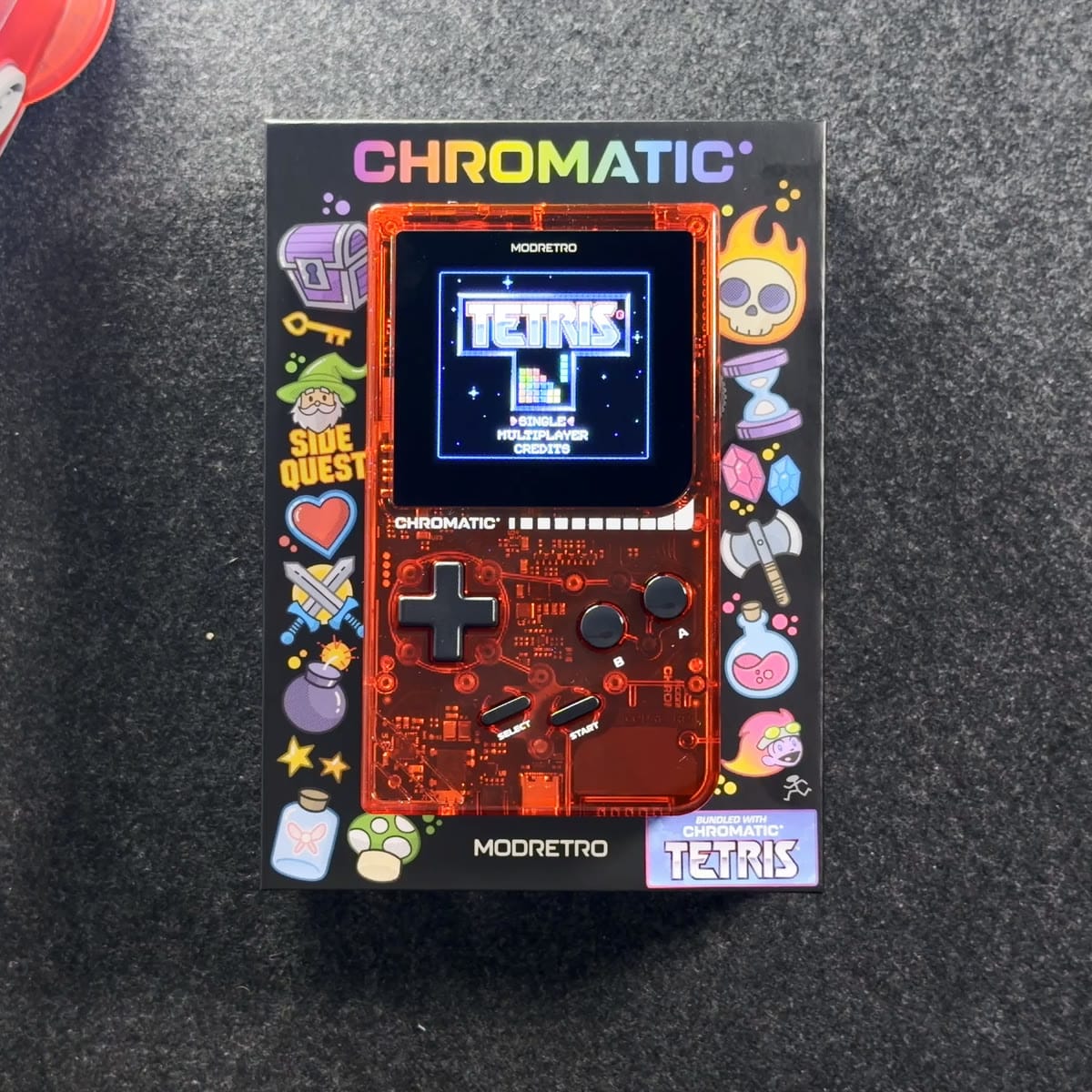 The transparent red ModRetro Chromatic box, with the console pictured on the front showing Tetris