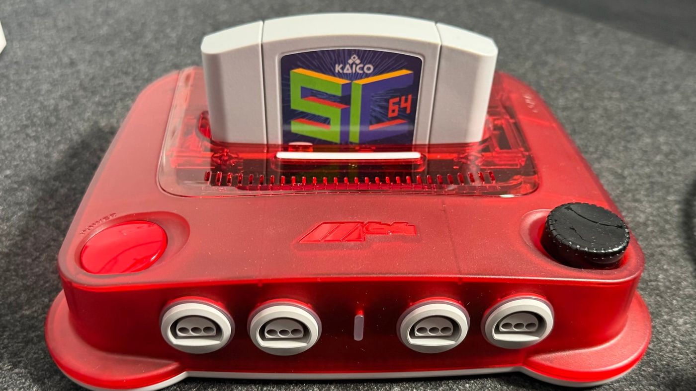 A grey SummerCart64 cartridge with a Kaico label plugged into a translucent red ModRetro M64 console