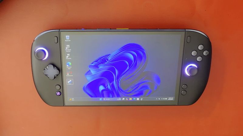 OneXPlayer X2 Mini Pro on a red mat, Windows desktop on screen and both stick lights glowing