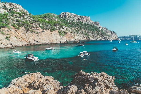 A boat on bright azure Mediterranean water by green hills in Mallorca
