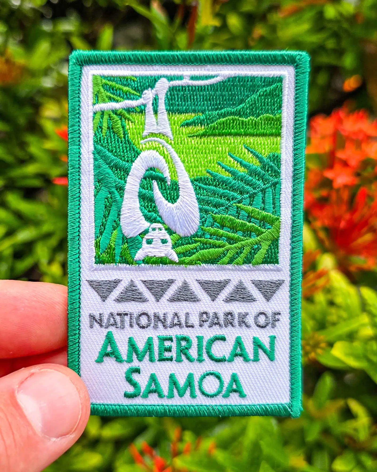 National Park of American Samoa embroidered patch held against tropical foliage background with green ferns and colorful plants