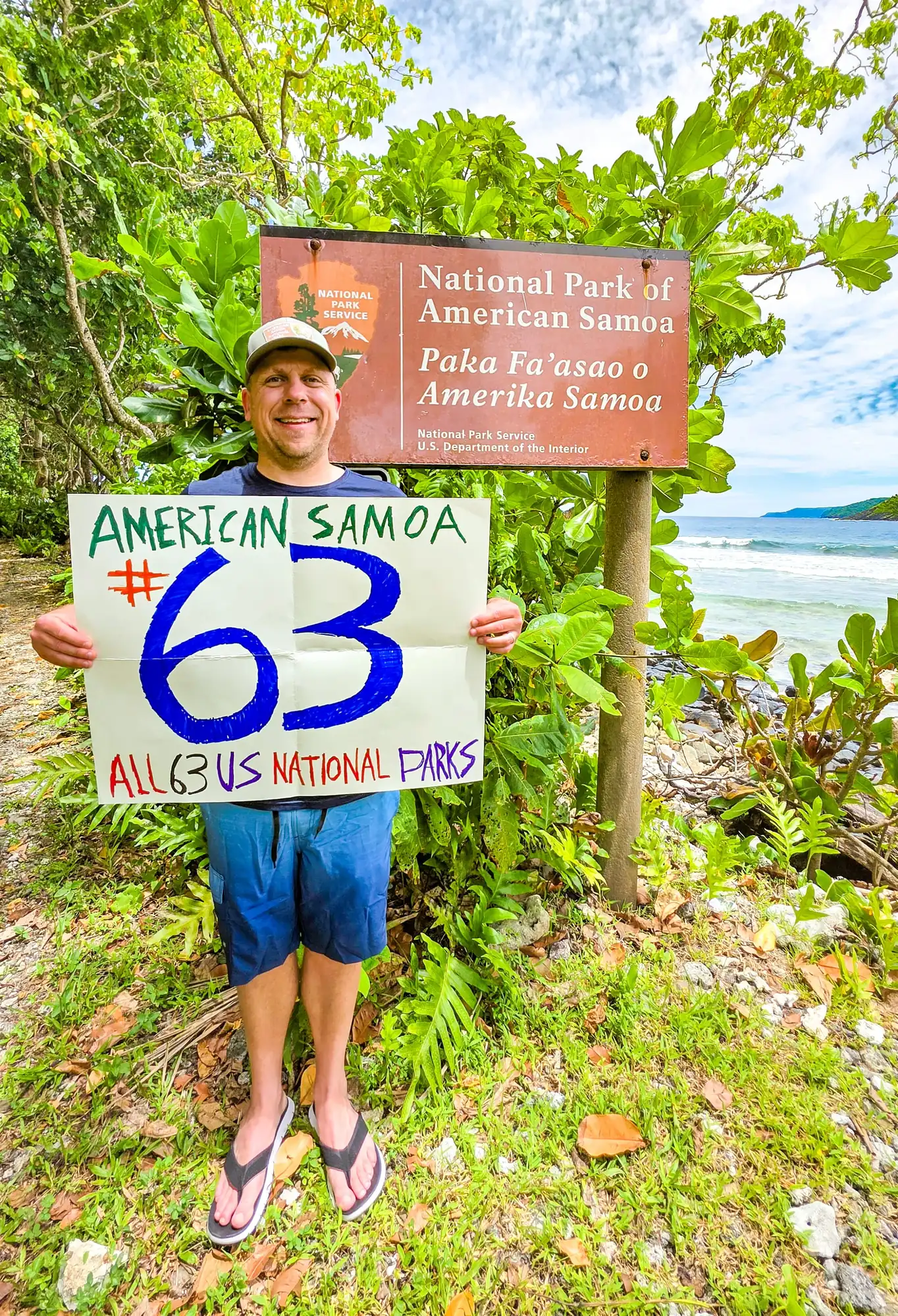 Eric Kufrin holding handmade sign reading American Samoa #63 All 63 US National Parks at National Park of American Samoa entrance