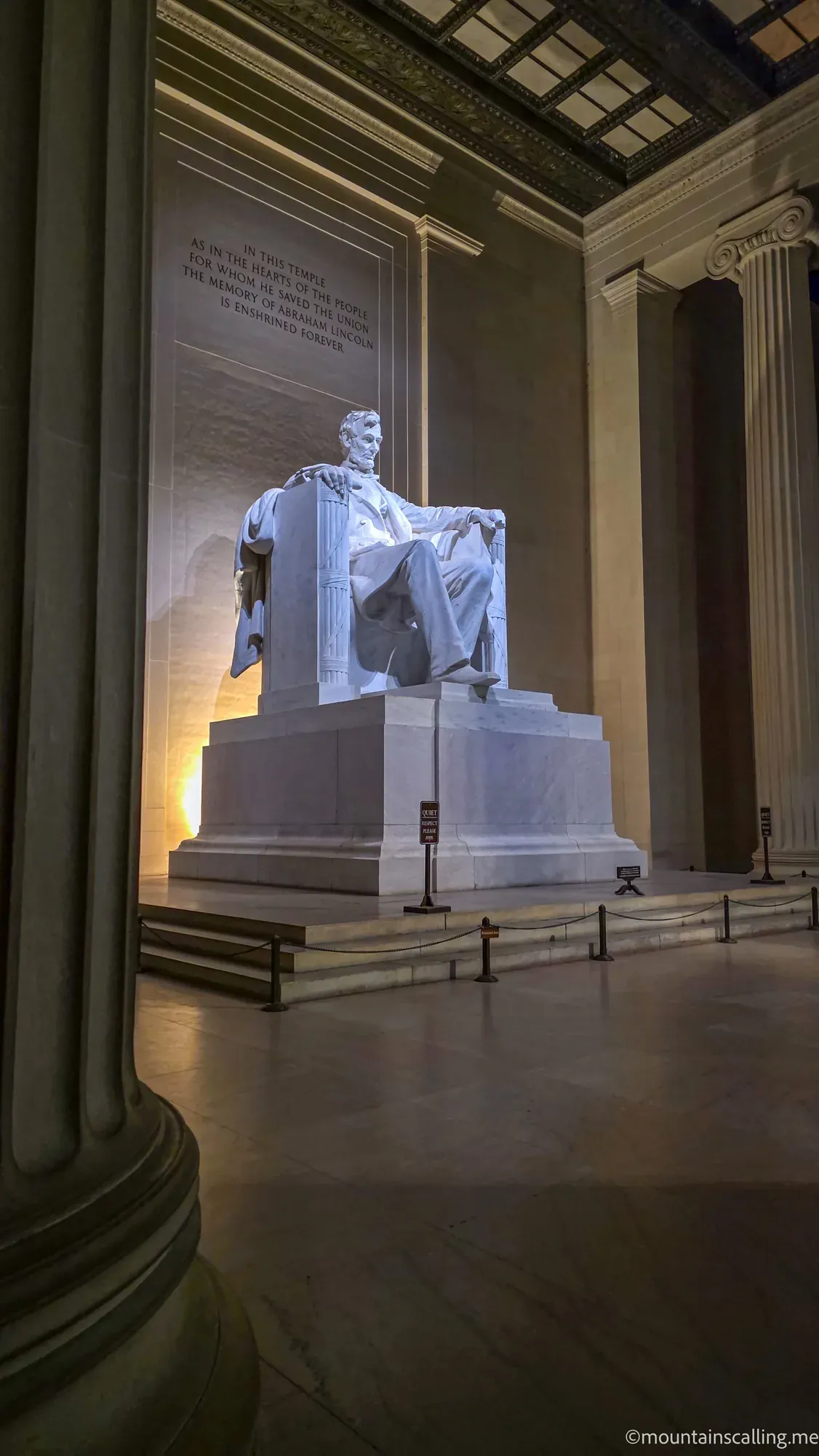 Abraham Lincoln statue seated in contemplation inside the Lincoln Memorial, illuminated by warm lighting with inscribed text visible on marble walls