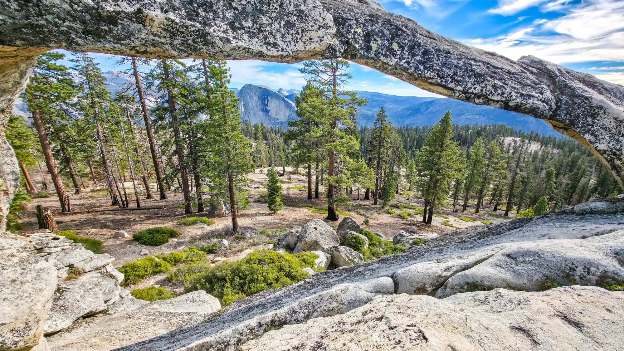 View through natural granite arch in Yosemite showing Half Dome and valley floor with pine trees