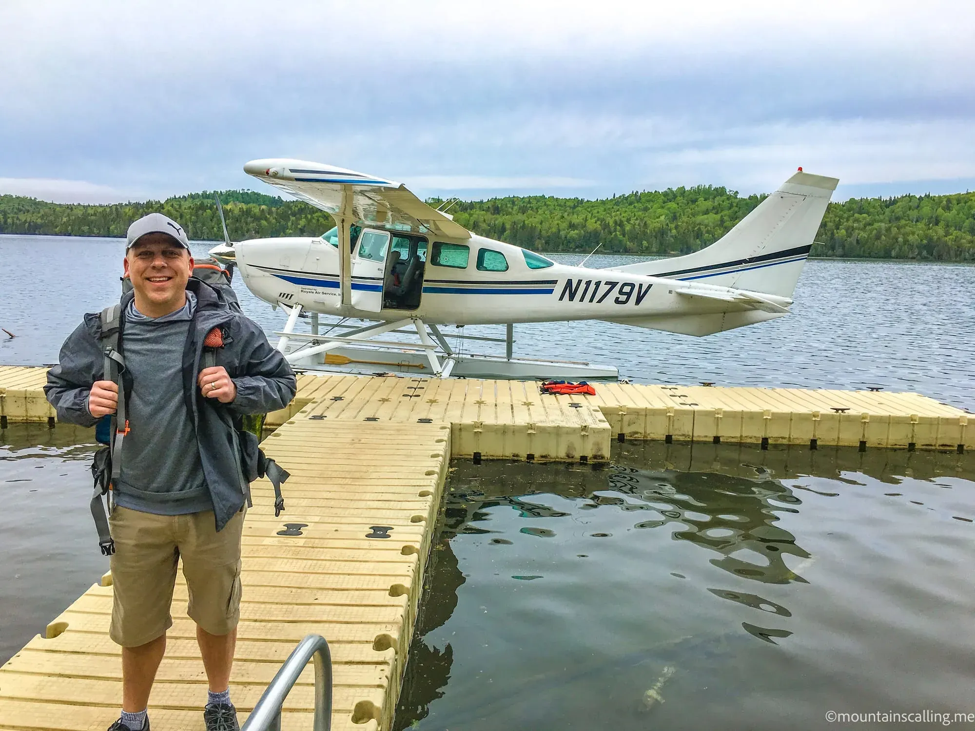 Eric Kufrin standing on wooden dock next to float plane at Isle Royale National Park with forested shoreline