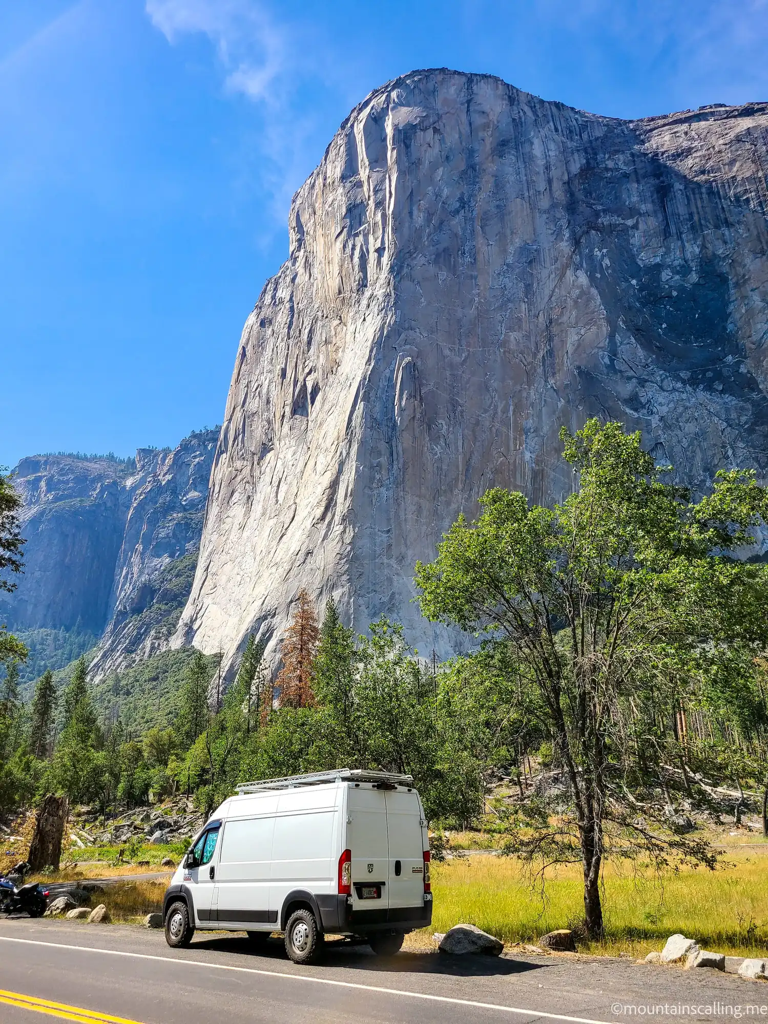 White van parked on road in Yosemite Valley with El Capitan's massive granite face towering above autumn trees