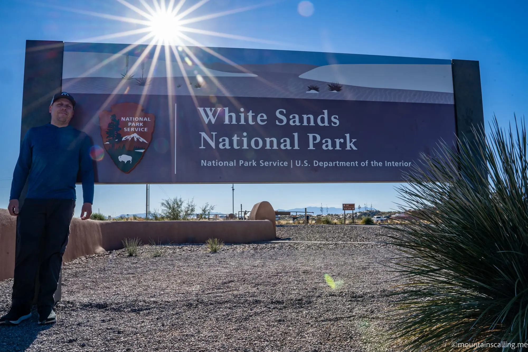 Eric Kufrin standing beside White Sands National Park entrance sign under bright desert sun with yucca plants