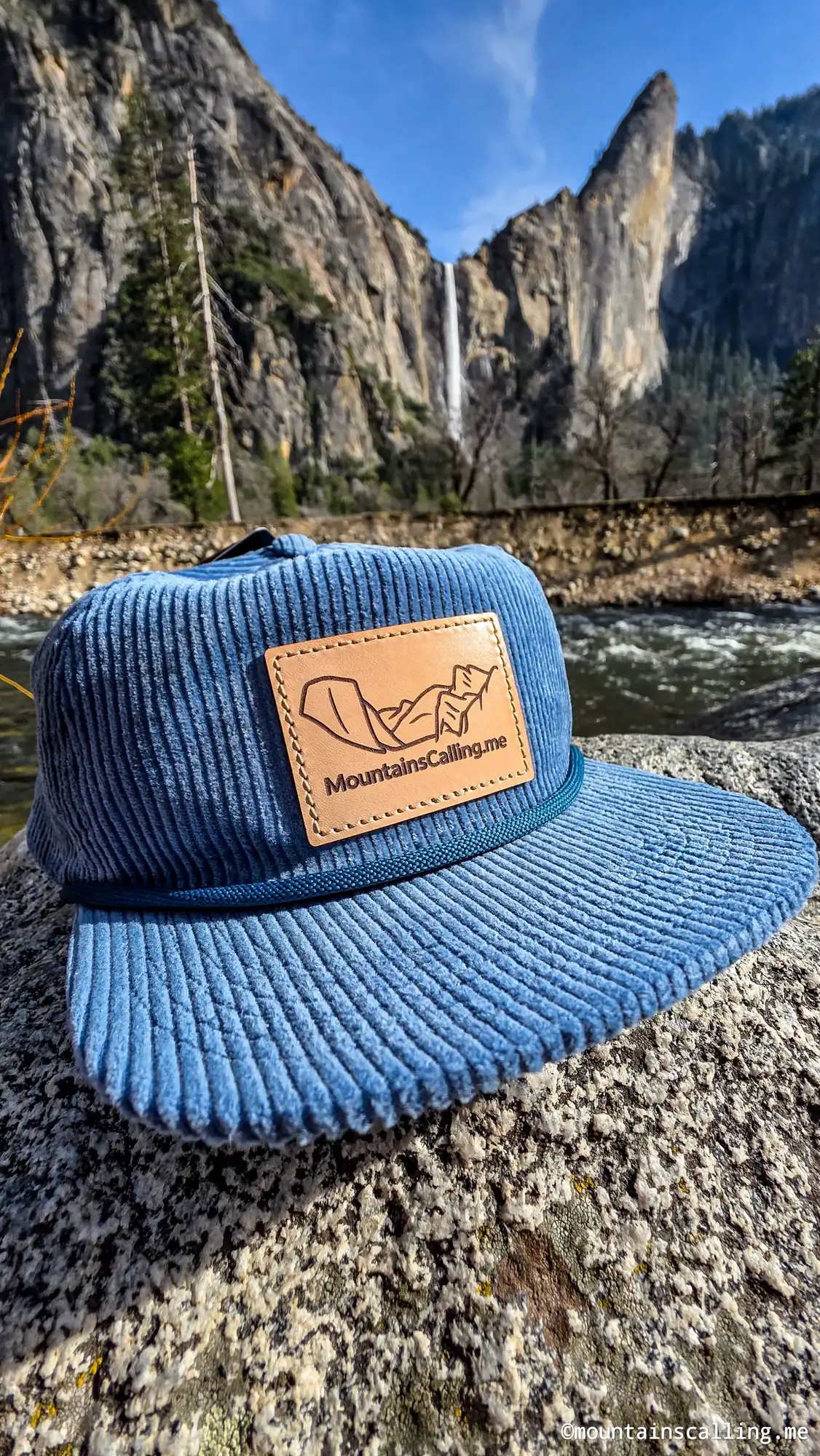 Blue corduroy hat on granite rock with Yosemite Falls waterfall and valley cliffs in background