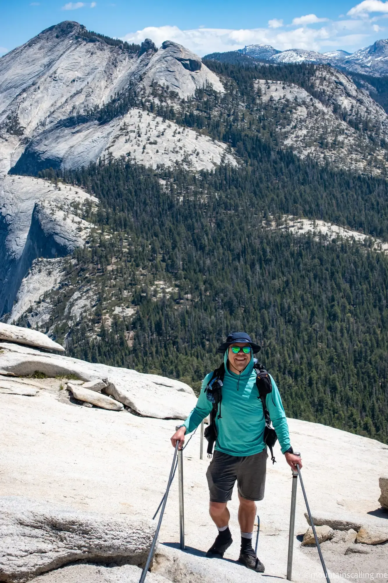 Eric Kufrin hiking with trekking poles on granite slabs in Yosemite National Park, wearing turquoise shirt and backpack with Half Dome visible in background