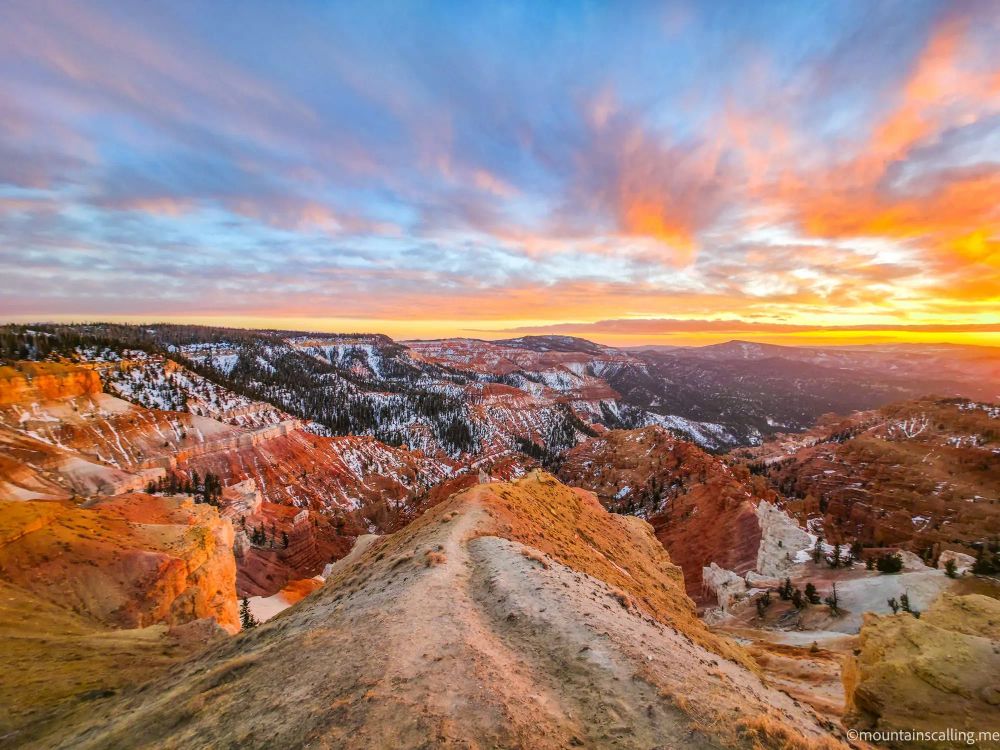Sunset over Cedar Breaks National Monument showing red rock hoodoos and snow-covered plateaus with dramatic orange and purple sky