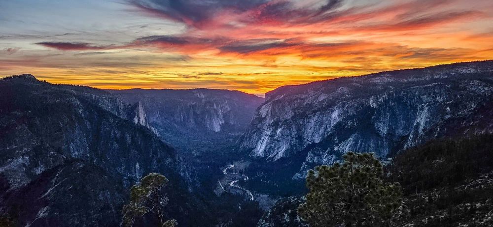 Dramatic sunset clouds over Yosemite Valley with granite cliffs and forested mountains in golden light