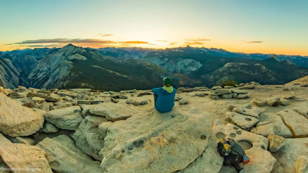 Professional Yosemite guide Eric Kufrin sitting on granite summit at sunset overlooking mountain wilderness with climbing gear nearby