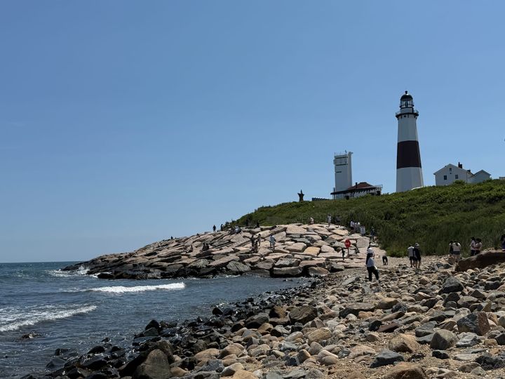 A photograph of the Montauk Lighthouse against a cloudless sky and a rocky shoreline