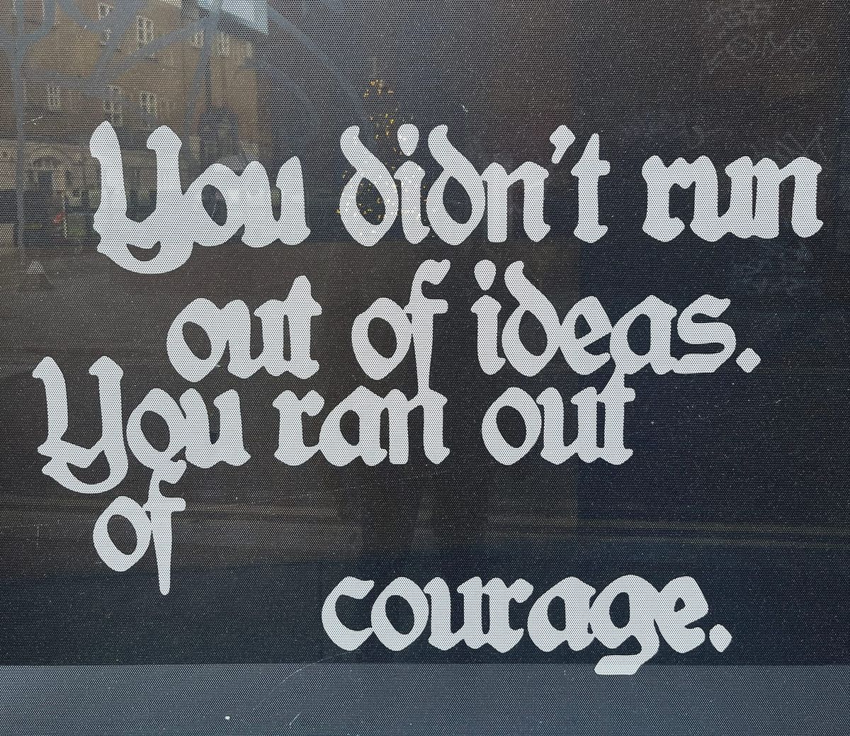 a shopfront window with the words “You didn’t run out of ideas. You ran out of courage.”