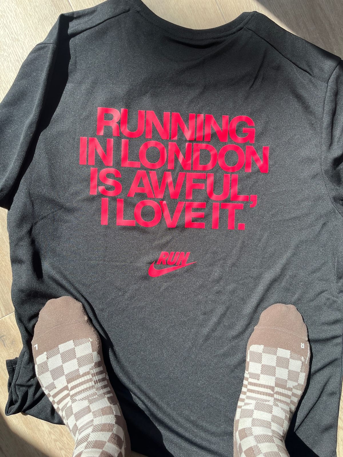 My cool running socks that are brown with a checkered pattern standing on top of a spread running t-shirt that reads Running in London is awful, I love it.
