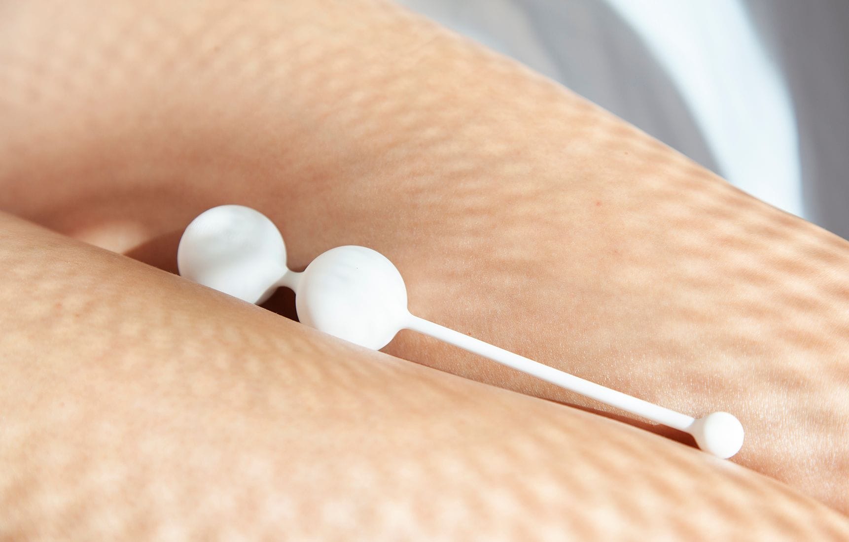 Bílé Venušiny kuličky Whoop·de·doo Light položené na kůži ženy s estetickou hrou stínů.