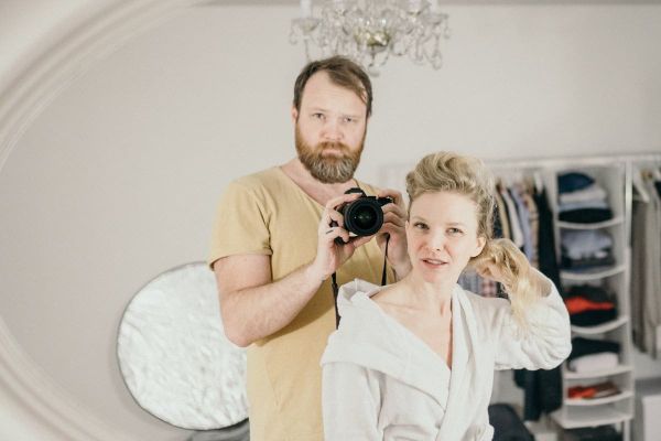 Fotograf s fotoaparátem a žena v bílém županu v interiéru.
