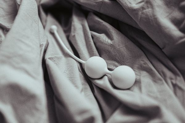 Černobílý detailní záběr na bílé venušiny kuličky Whoop·de·doo položené na zmačkané šedé látce. Snímek zdůrazňuje texturu a minimalistický design.