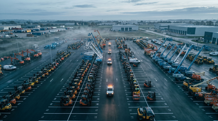 Aerial view at dawn of an equipment-rental depot: orderly rows of machinery with service vehicles moving between them.