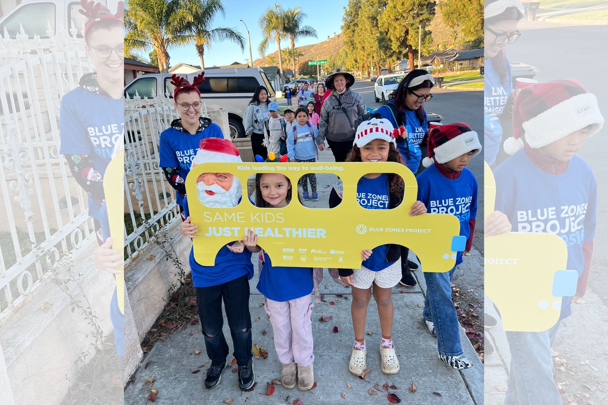 A group of elementary school students walk together holding a yellow "Walking School Bus" banner during a Blue Zones walk-to-school event.