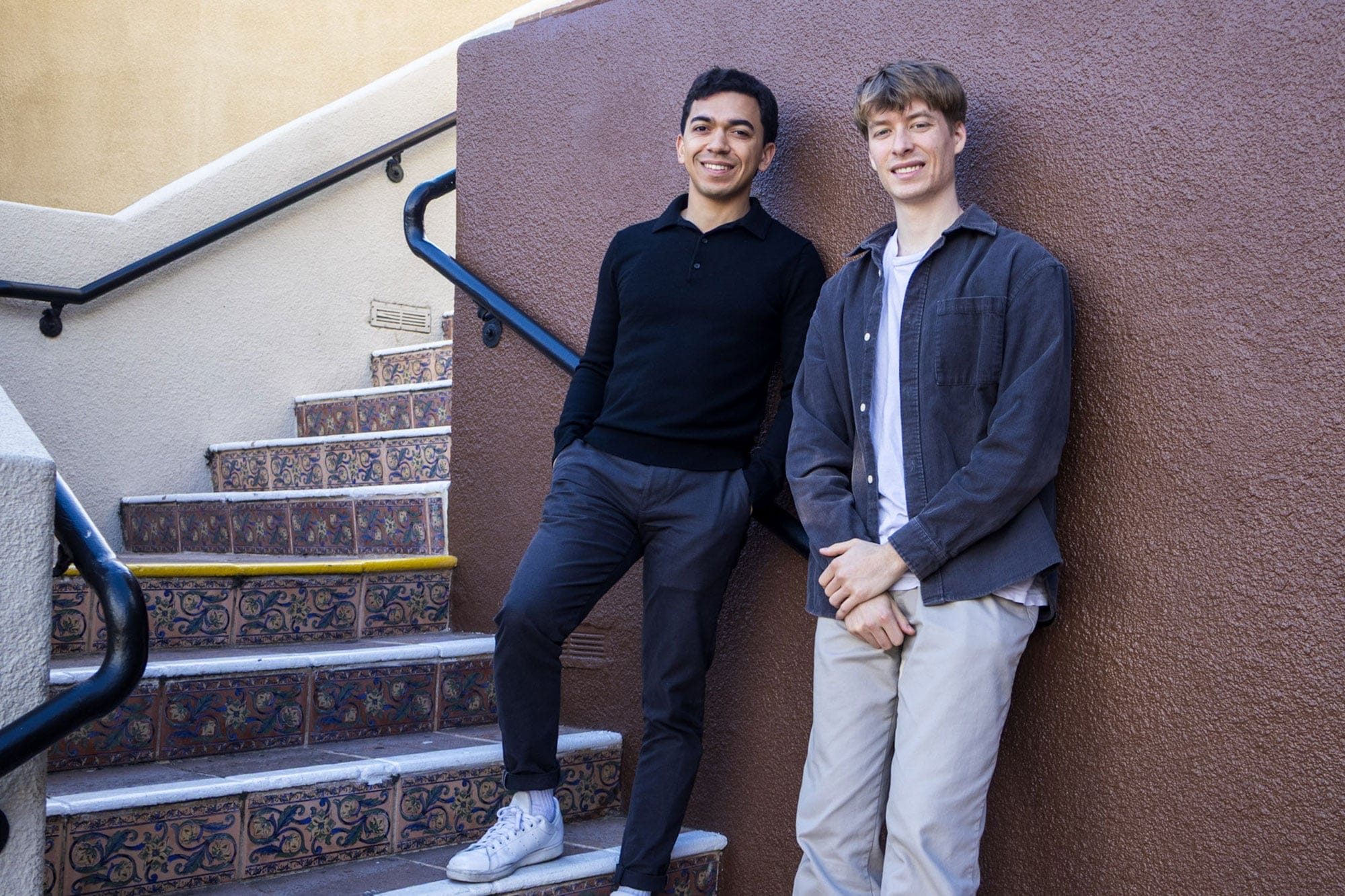 Miles Ward and Blake Skrable smiling while leaning against a wall beside tiled outdoor stairs