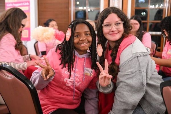 Two smiling middle school girls in pink shirts flash peace signs at the Day of the Girl event.