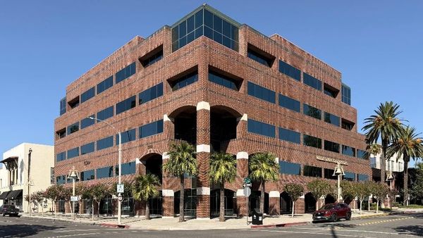 A multistory brick office building with arched entrances, palm trees, and a street-corner sidewalk out front.
