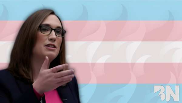 An image of Sarah McBride wearing a pink blouse and navy blue blazer in front of a trans pride flag with the Burns Notice flames superimposed underneath.