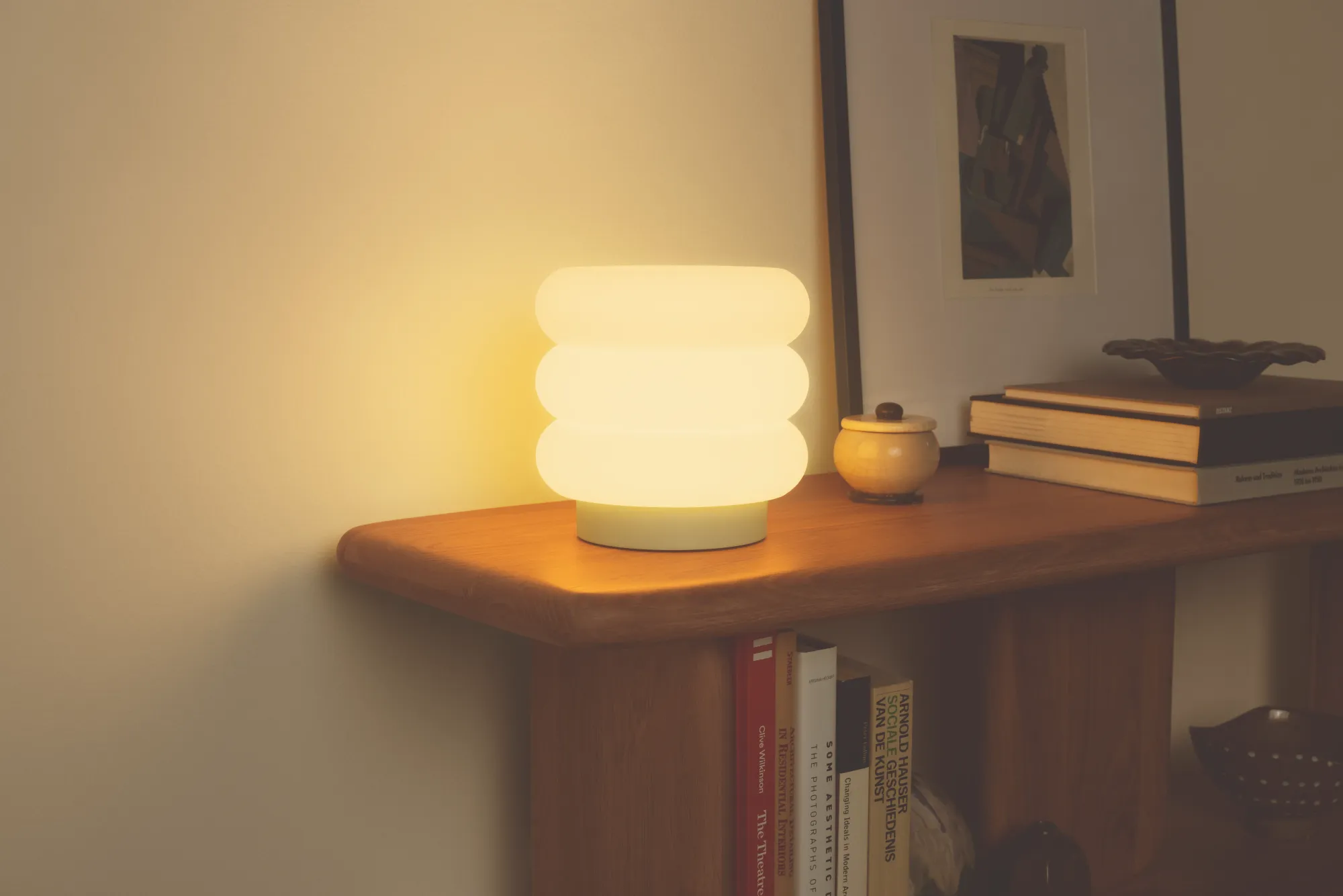 The Argizari Table Light illuminates a wooden table filled with several books and several pieces of table decor.