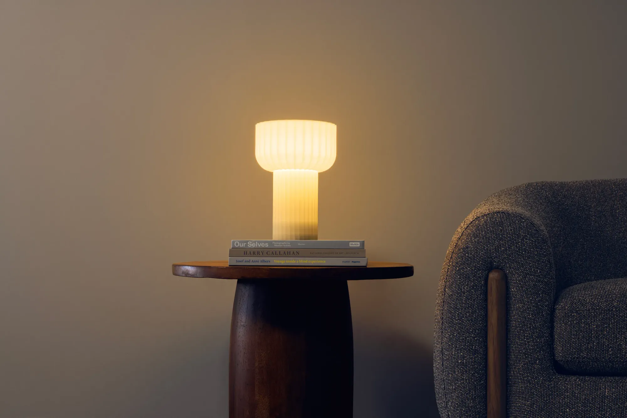 The Word Table  Lamp by Gantri lights up the room, aesthetically placed above three coffee table books on a couch’s side table.