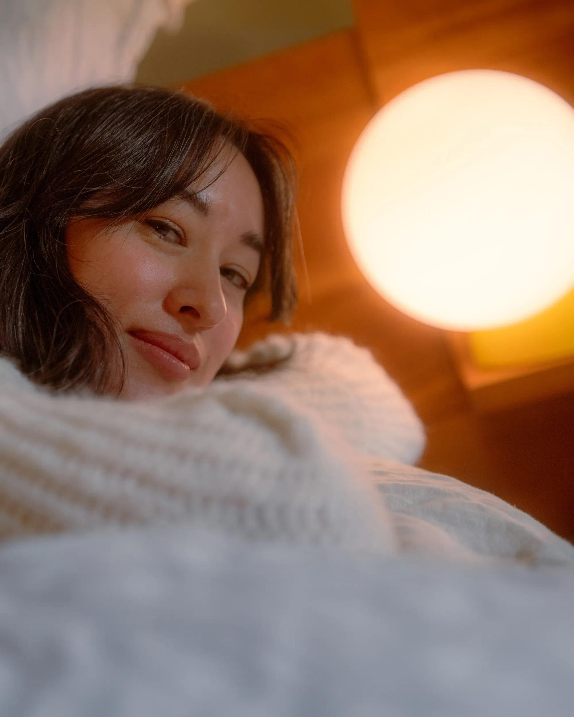 A woman dressed in a woolen sweater smiles at the camera. A light from Gantri lights up her face