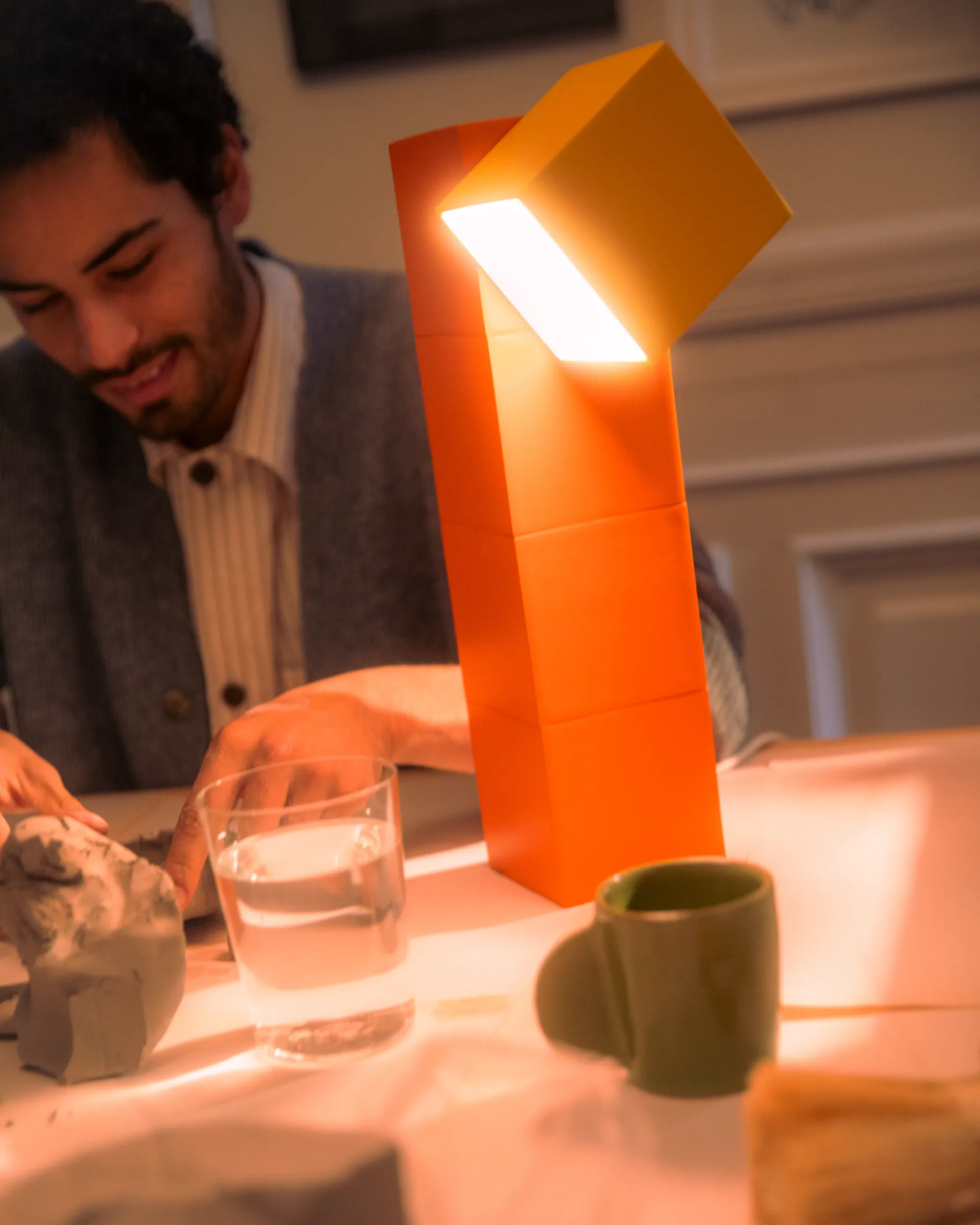 A man is sculpting something out of clay. He is being guided by light from a Gantri Analog Table Top Light.