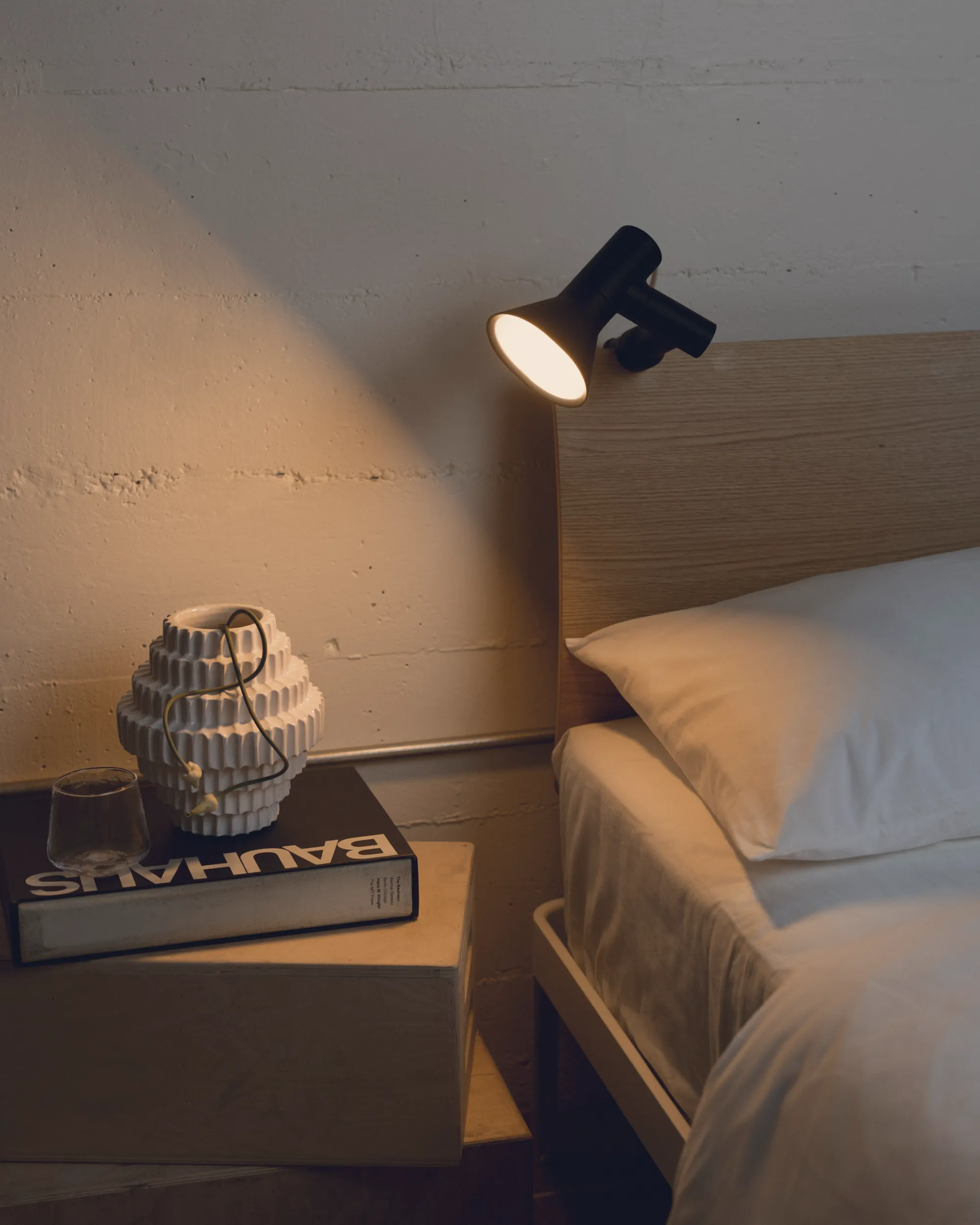 A bedside area with some books is illuminated by a Gantri Clamp Light