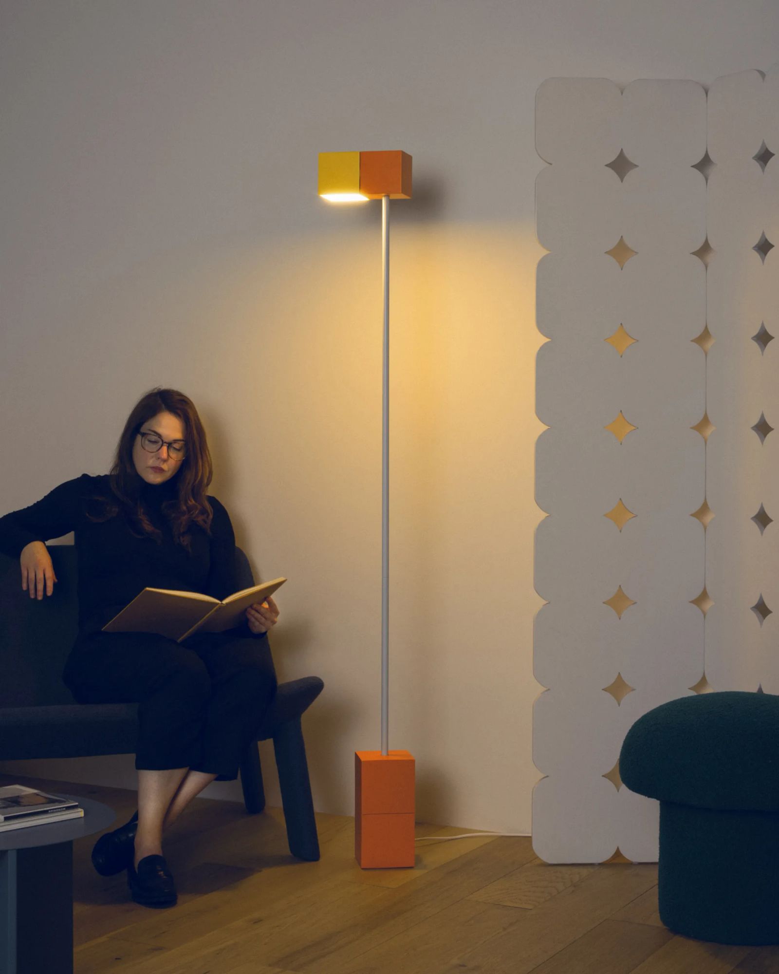 A woman sits on a chair reading a book with the help of the light from Gantri’s Analog Floor Lamp.
