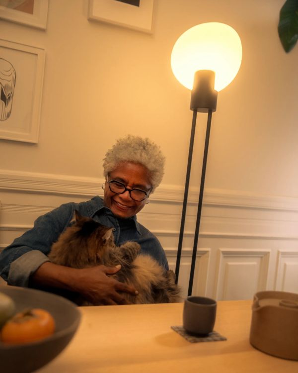 An elder woman is smiling in joy while holding her fluffy black cat.