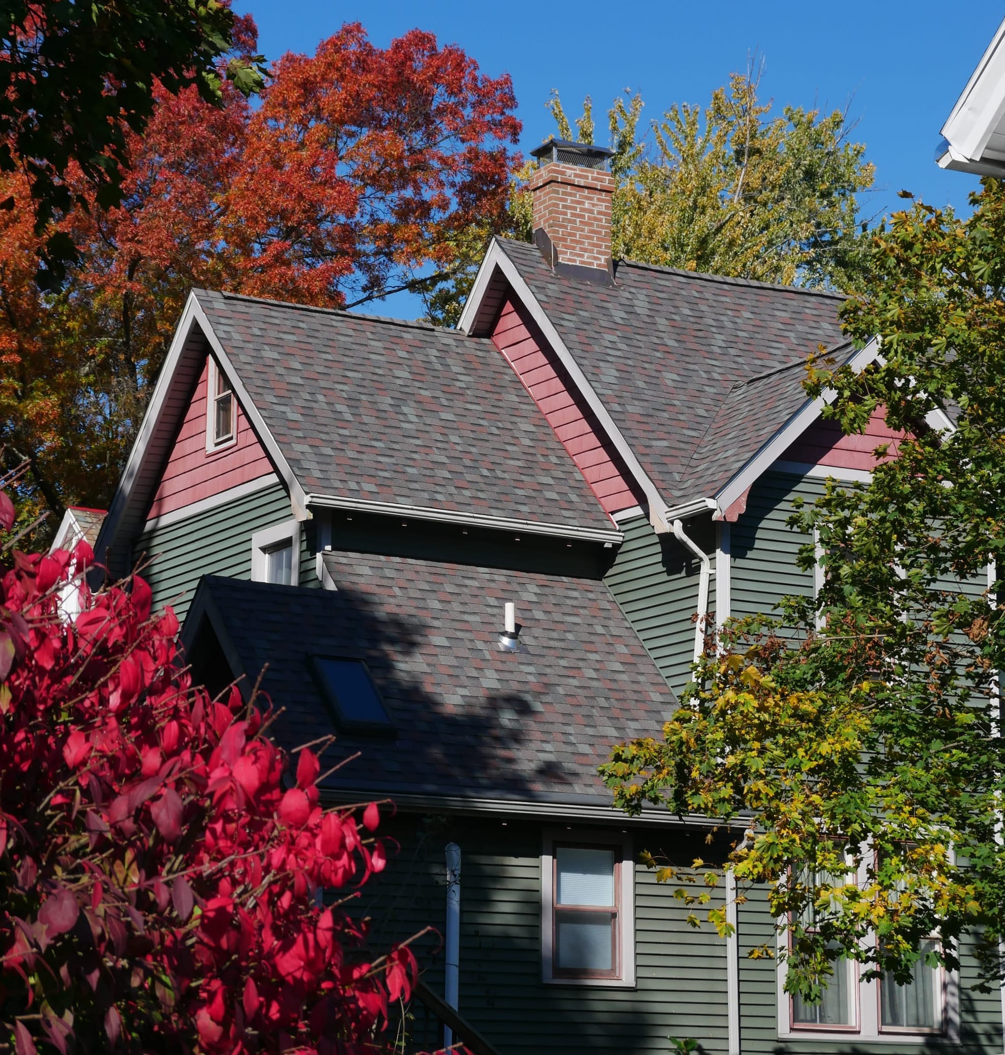 A rear view of a green and pink house with multiple leveled roof peaks