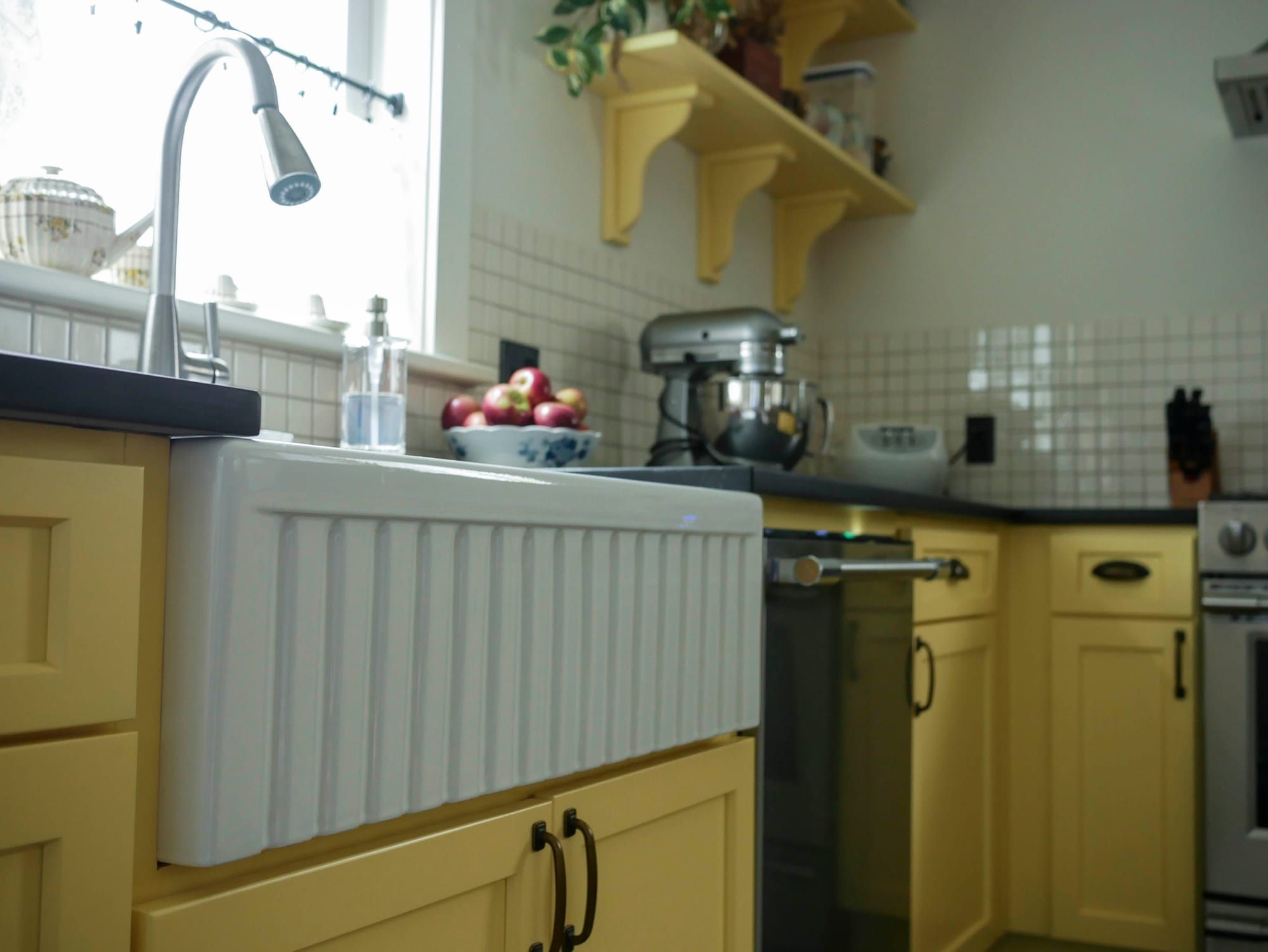 A white enamel fluted sink sits mounted below the counter next to yellow cabinets