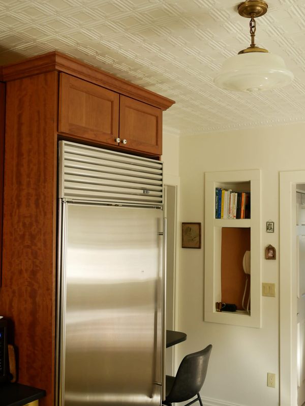 A stainless steel Subzero refrigerator in a cherry wood build-out cabinet, a phone nook on an ivory painted wall in the background