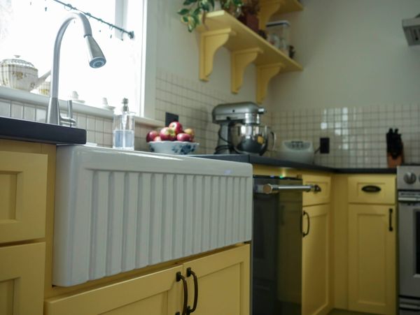 A white enamel fluted sink sits mounted below the counter next to yellow cabinets