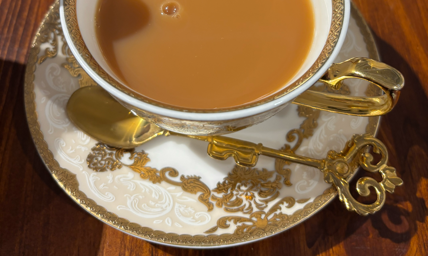 Hot tea in a fancy teacup and saucer, with a gold spoon shaped like key next to it.