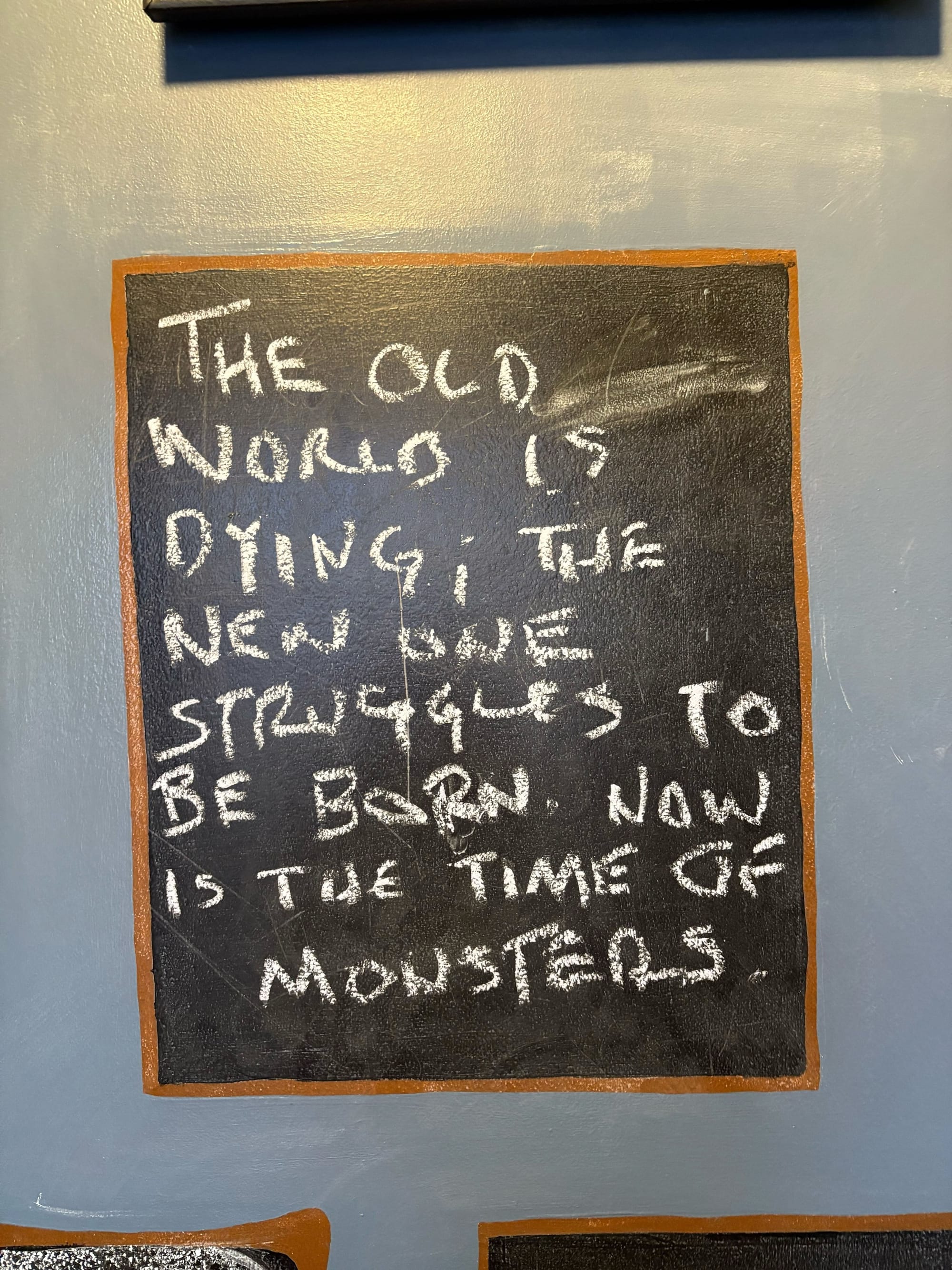 a chalk board that says "the old world is dying; the new one struggles to be born. Now is the time of monsters"