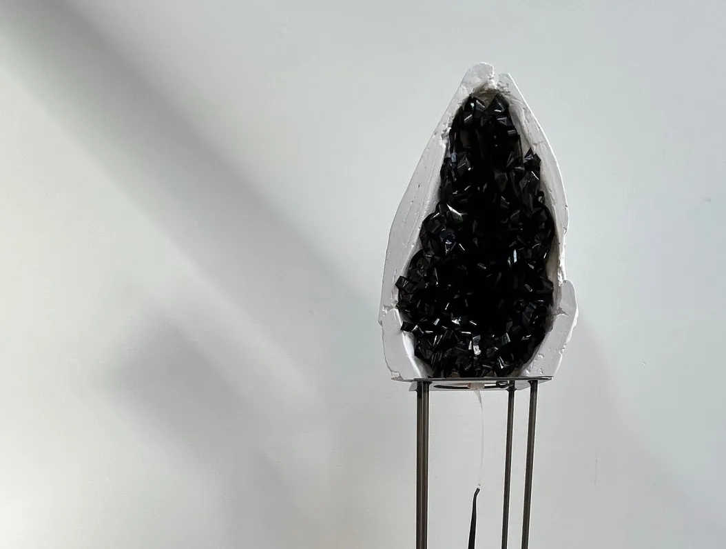 a sculpture that looks like a geode on a stand, against a white wall