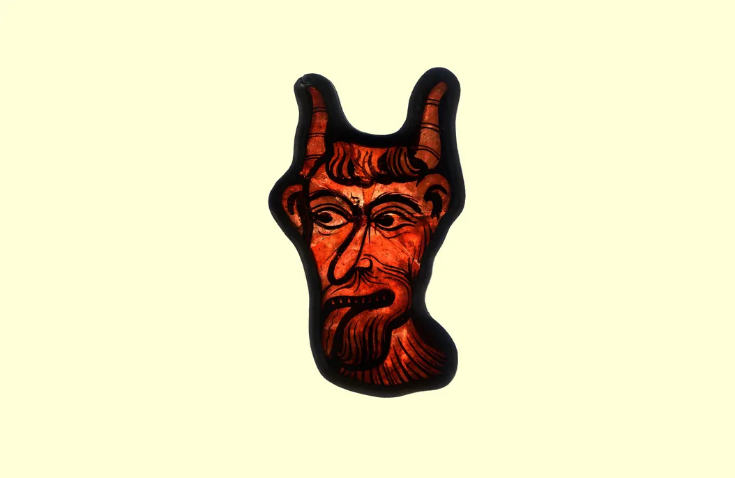 A piece of red stained glass painted to look like the devil sticking his tongue out.
