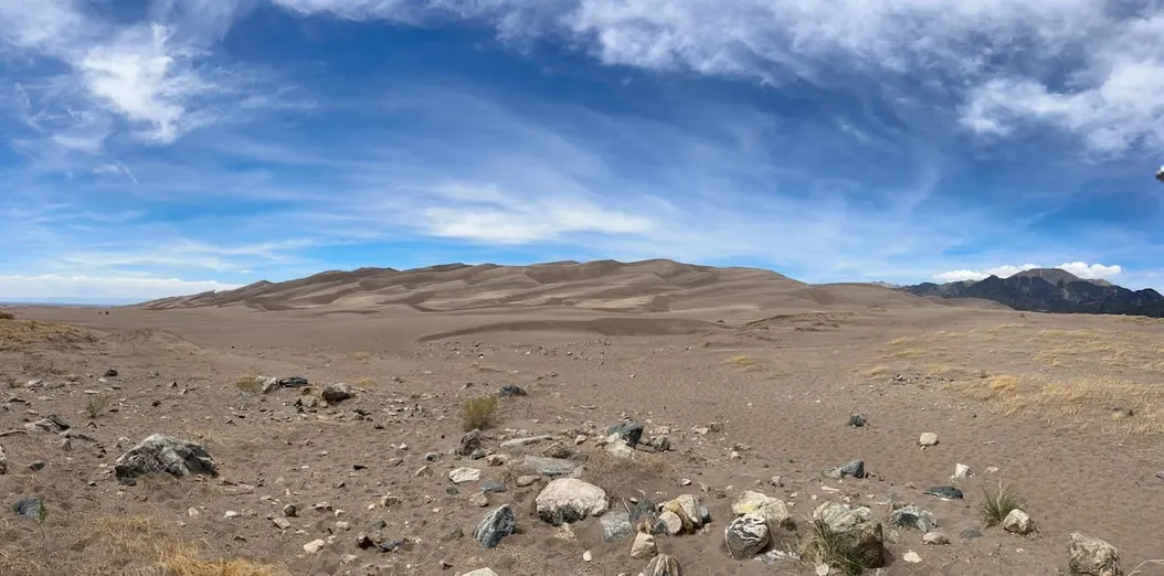 A series of sand dunes against a blue sky with whispy clouds.
