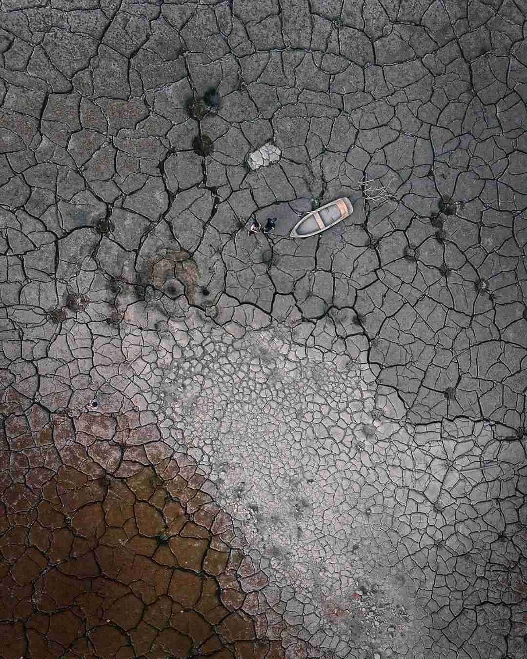 Two people are standing by the boat in the lakebed.