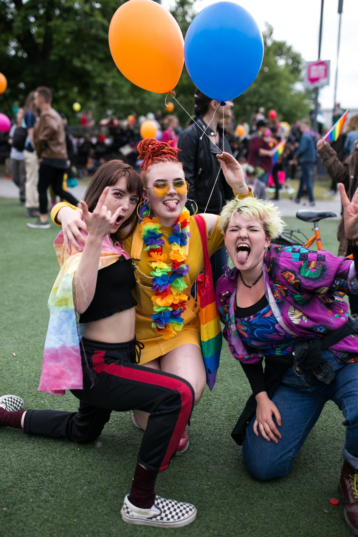people posing and carrying balloons in front of camera at a pride parade