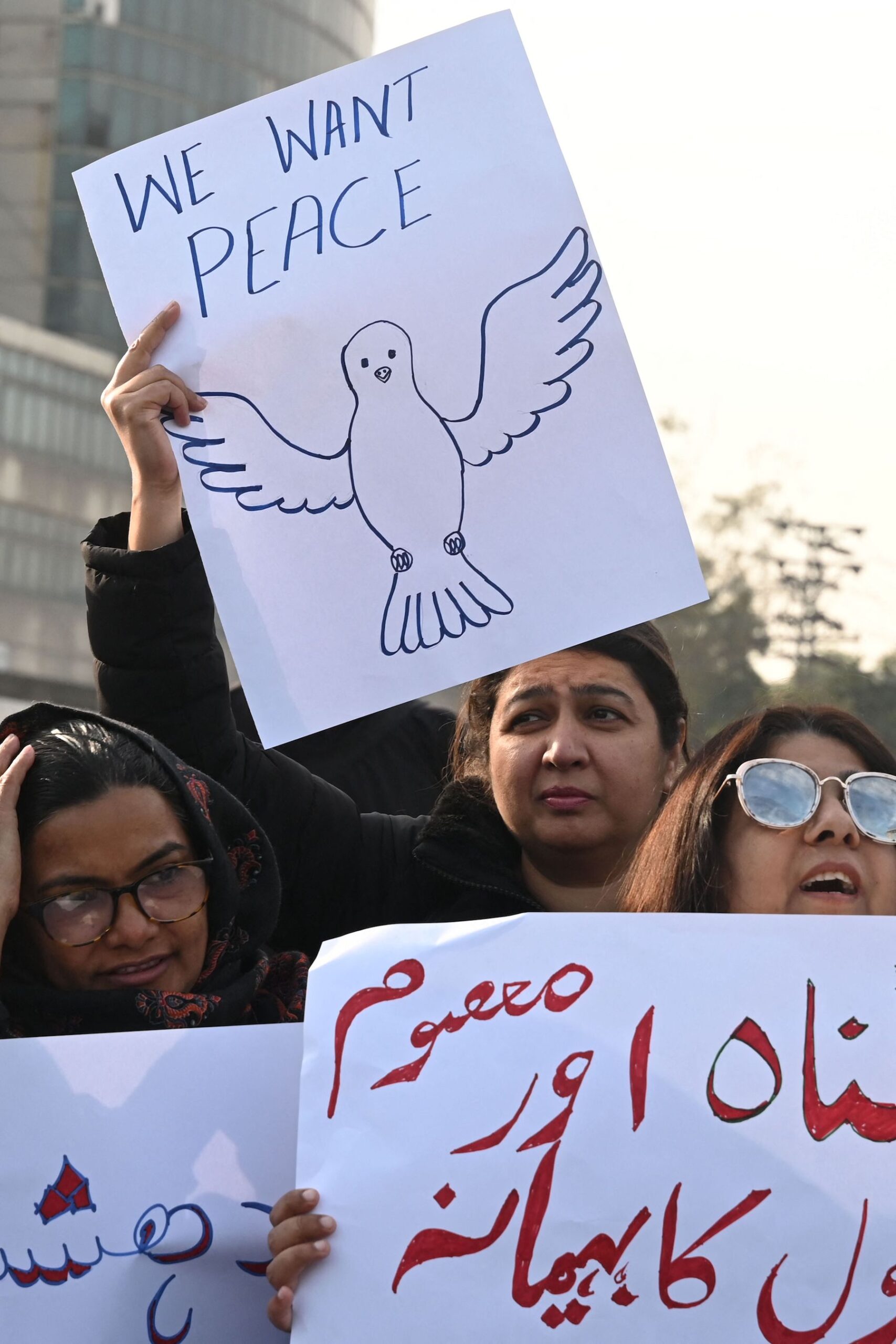people holding signs "we want peace" protesting on the street